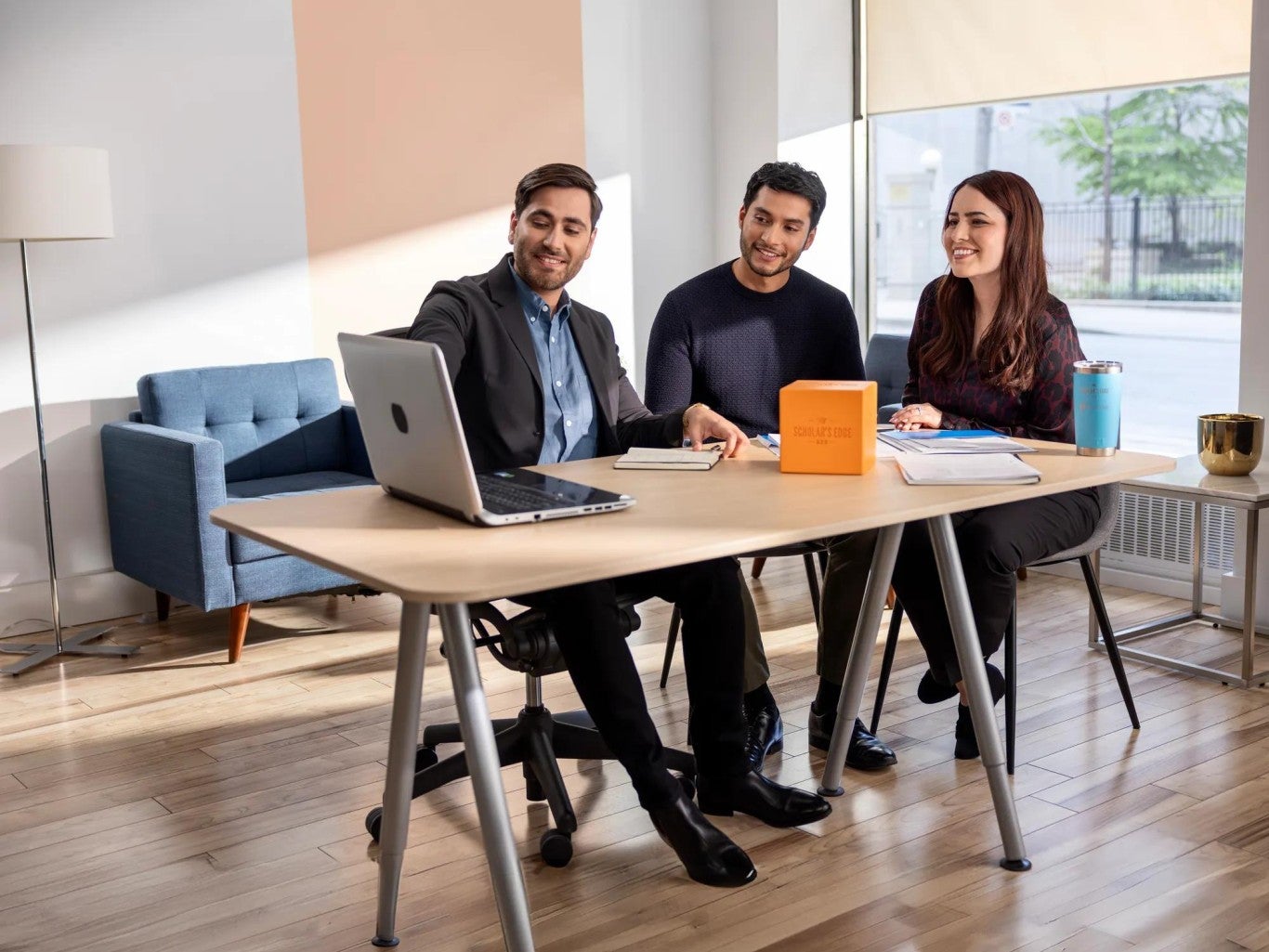 A financial professional and a couple reviewing information on a computer. The Scholar's Edge Cube is on the table.