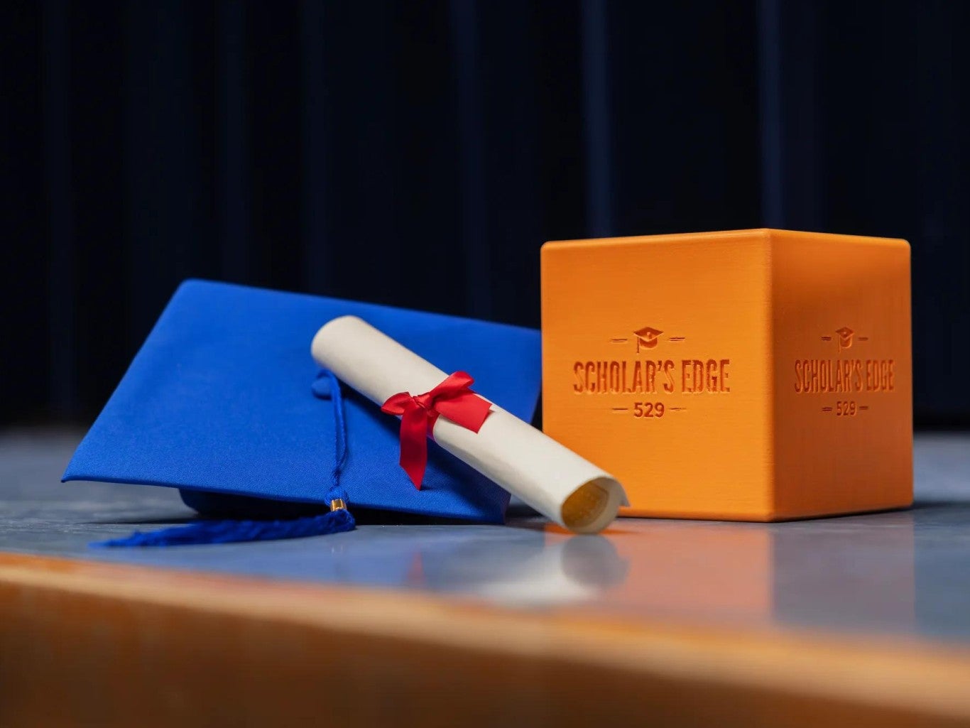 The Scholar's Edge Cube is on a table with a graduation cap and diploma.