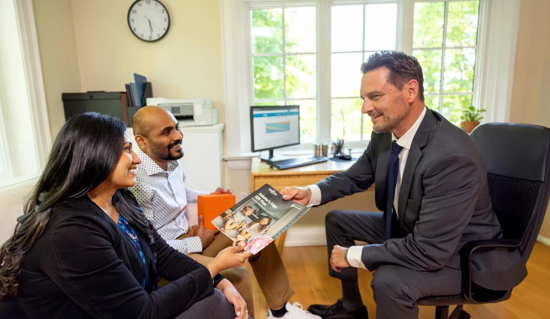 Couple sitting with their financial professional in an office being handed a brochure.