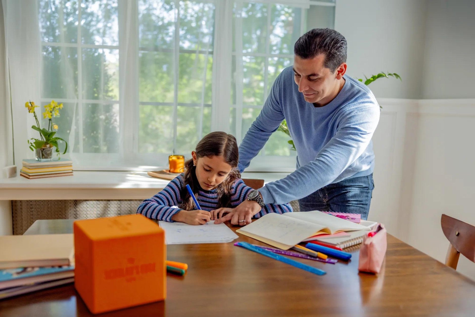 A father helping his daughter with her school work. The Scholar's Edge Cube is on the table.